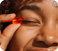 Close-up of a smiling person holding a red capsule pill near their eye.