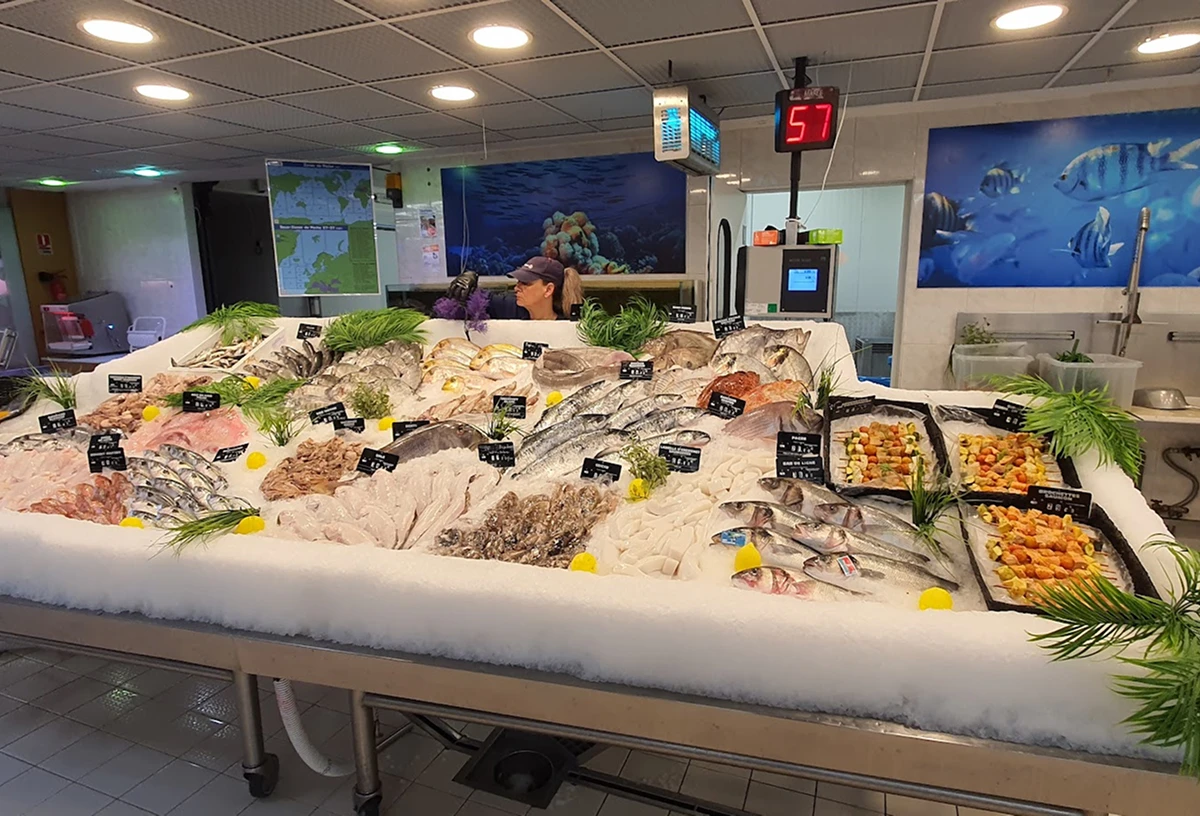 Étal de poisson bien garni avec divers poissons frais, fruits de mer et garnitures, sous un éclairage intérieur.