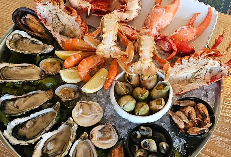 Plateau de fruits de mer avec homard, crevettes, huitres, palourdes, escargots de mer et crevettes grises sur un lit de glace.