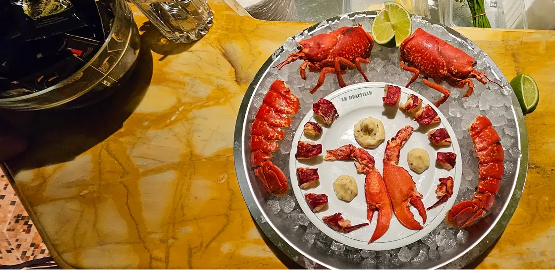 Plat de homard décoquillé avec morceaux de chair et sauces, servi sur un lit de glace avec quartiers de citron vert.