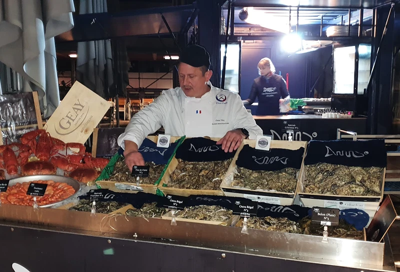 Dave Vitré présente un étal de fruits de mer avec des huîtres, des crevettes et des homards dans un marché intérieur.