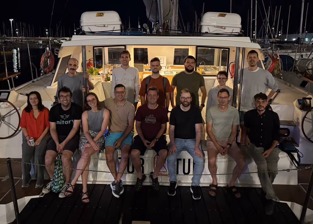 Group of 14 people posing and smiling on a docked boat at night.