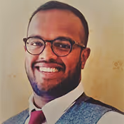 Smiling man with beard and glasses wearing a suit and tie.