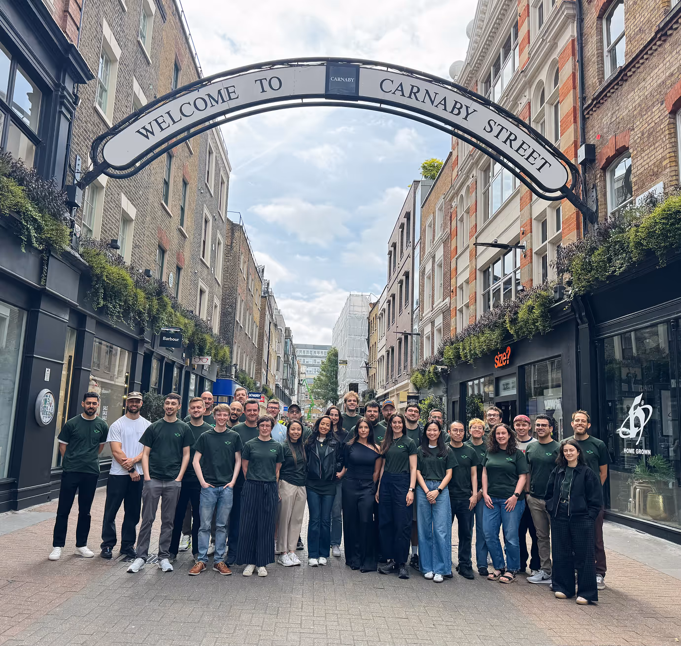 Group of people standing under a Carnaby Street welcome sign in a narrow city street.