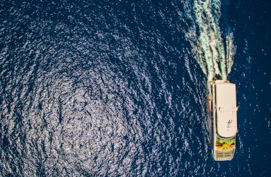 Aerial view of a Cat Cocos ferry sailing through deep blue ocean, leaving a foamy trail behind as it travels across sunlit water.