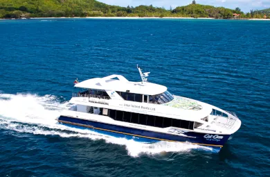 Cat Cocos high-speed ferry "Isle of La Digue" sailing near a lush green Seychelles island, cutting through the deep blue ocean with white wake.