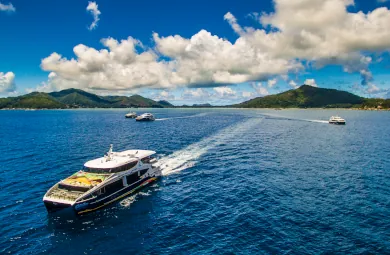 Multiple Cat Cocos ferries sailing between the Seychelles islands under a vibrant blue sky with scattered clouds and green mountainous landscapes.