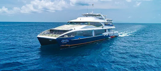 Cat Cocos ferry cruising across calm blue ocean under a partly cloudy sky, viewed from a front-side angle.