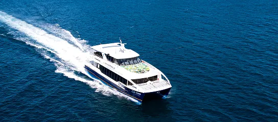 Cat Cocos ferry speeding through deep blue ocean waters, leaving a long white wake behind.