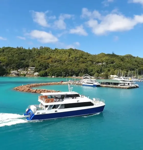 Cat Rose ferry departing from the jetty at Baie Sainte Anne on Praslin Island, surrounded by turquoise water and lush green hills.