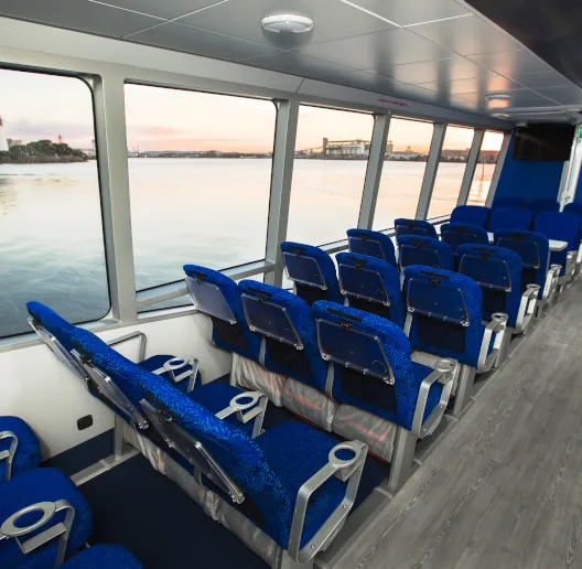 Interior of the main cabin on a Cat Cocos ferry with blue cushioned seats and large windows overlooking the sea.