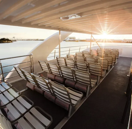 Upper deck seating area on a Cat Cocos ferry at sunset, with rows of open-air seats and partial roof cover.