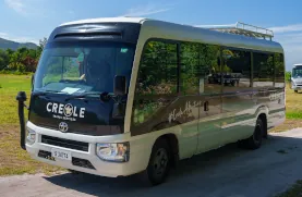 Silver and black minibus labeled Creole parked on a sunny road by grassy hills.