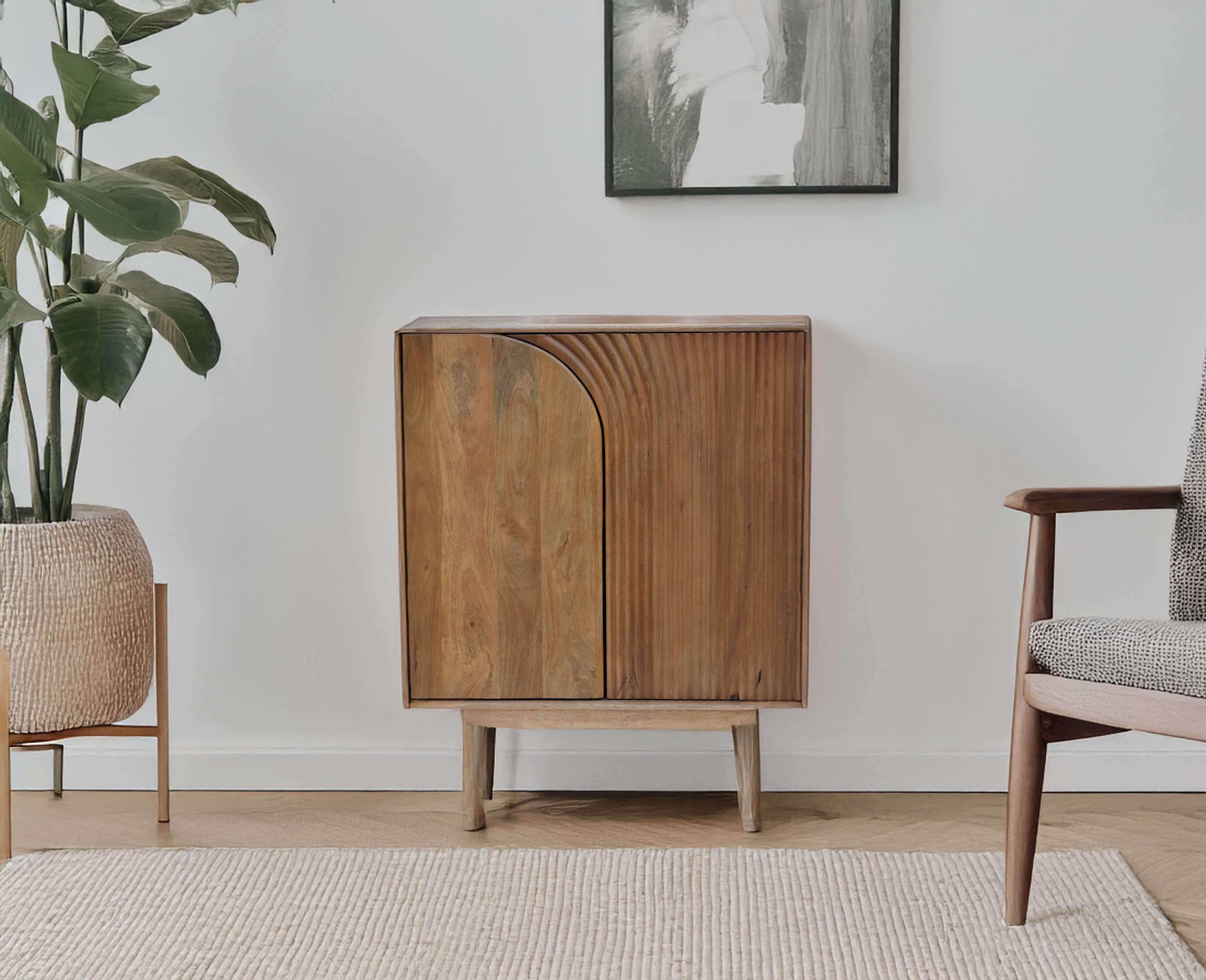 Modern wooden cabinet with arched groove design, placed against a white wall beside a potted plant and wooden armchair.