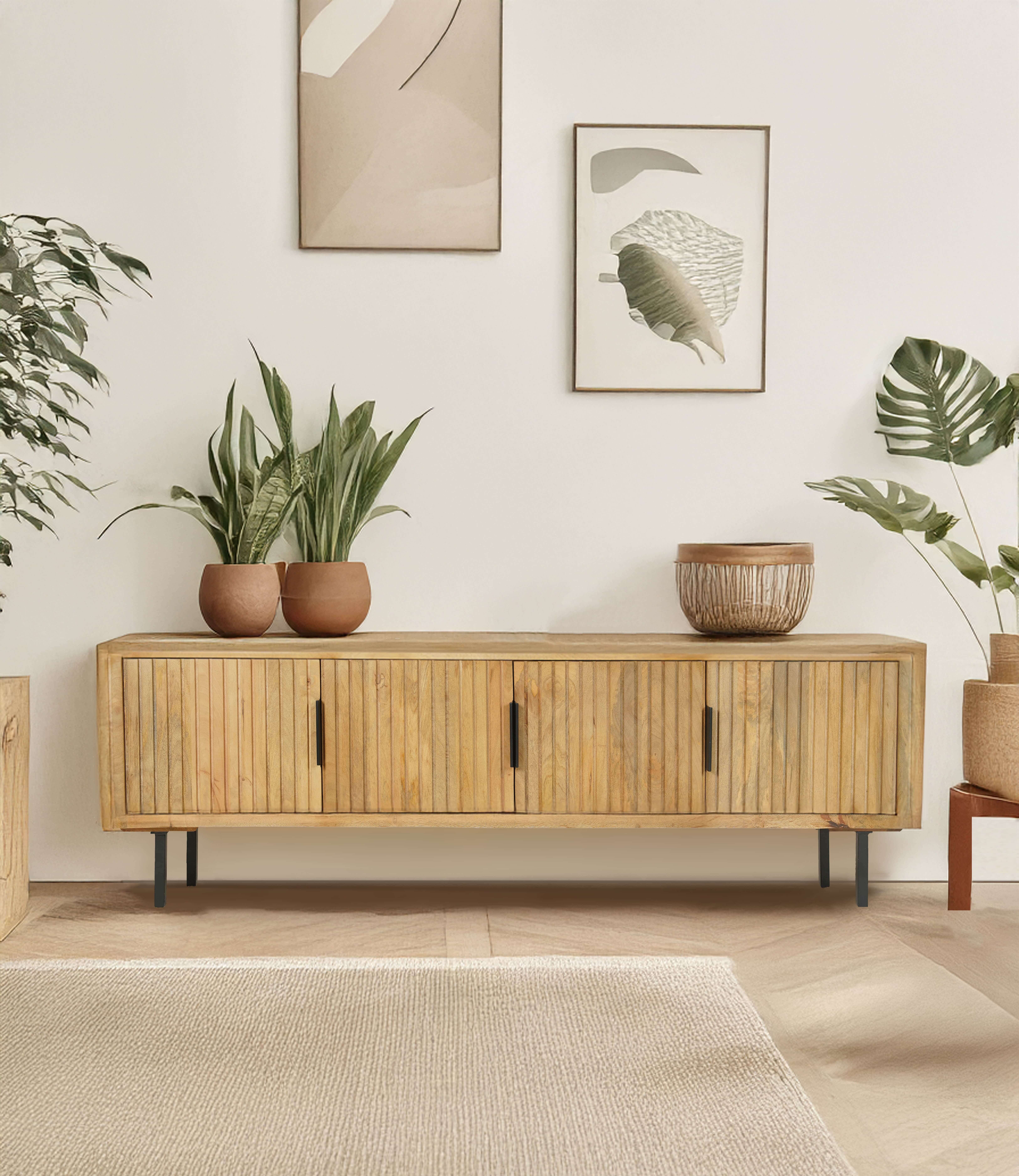 Minimalist wooden sideboard with vertical slats, black metal legs, and potted plants on top, set against an off-white wall with abstract art.