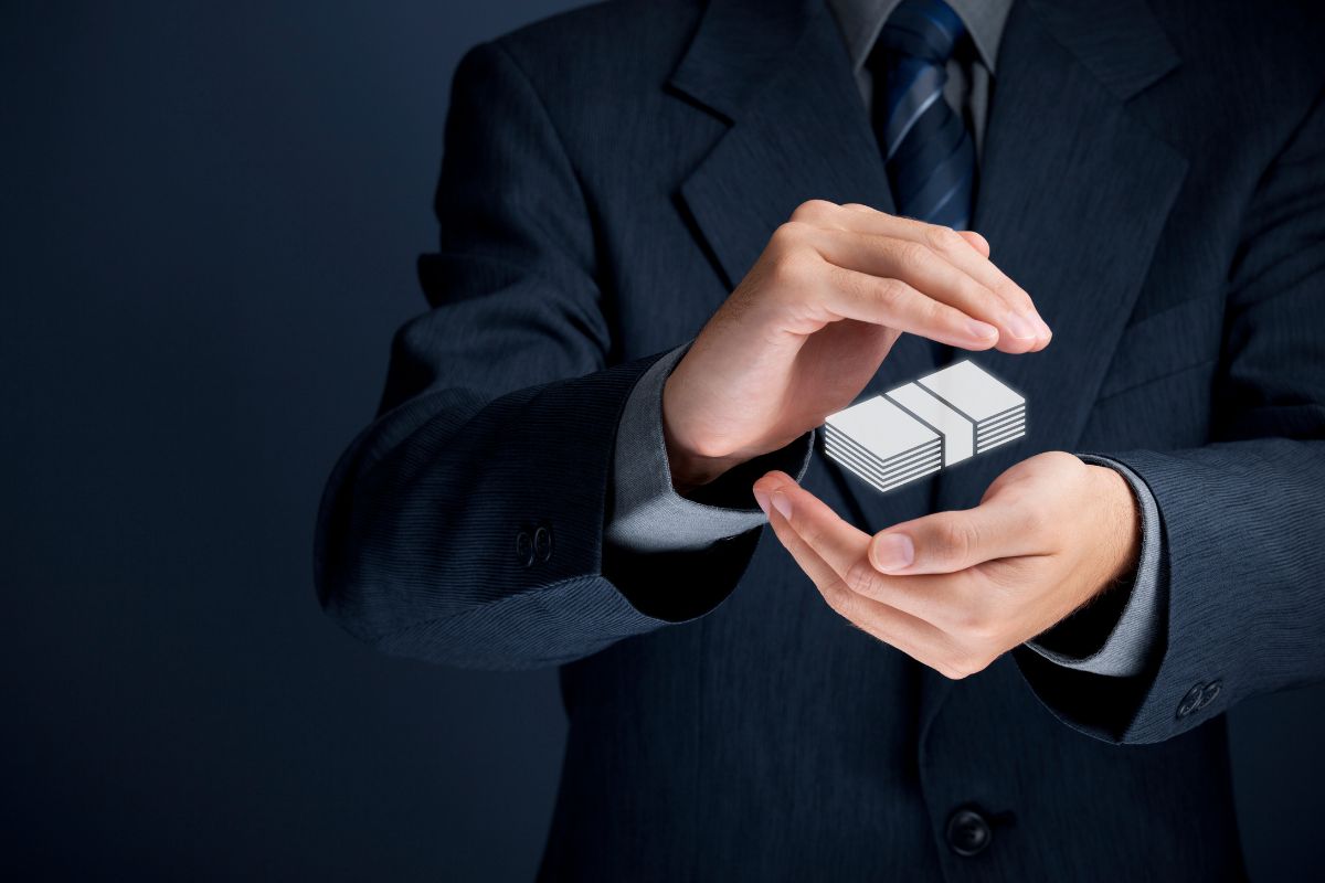 Man in suit with hands cupped around a stack of money as if protecting it