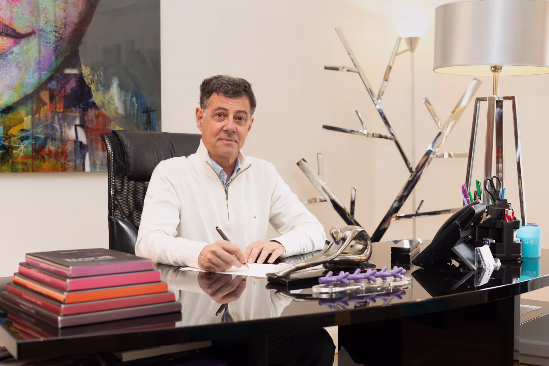Dr. Foumenteze - Homme médecin assis  à son bureau tenant un stylo main droite, avec un pull blanc