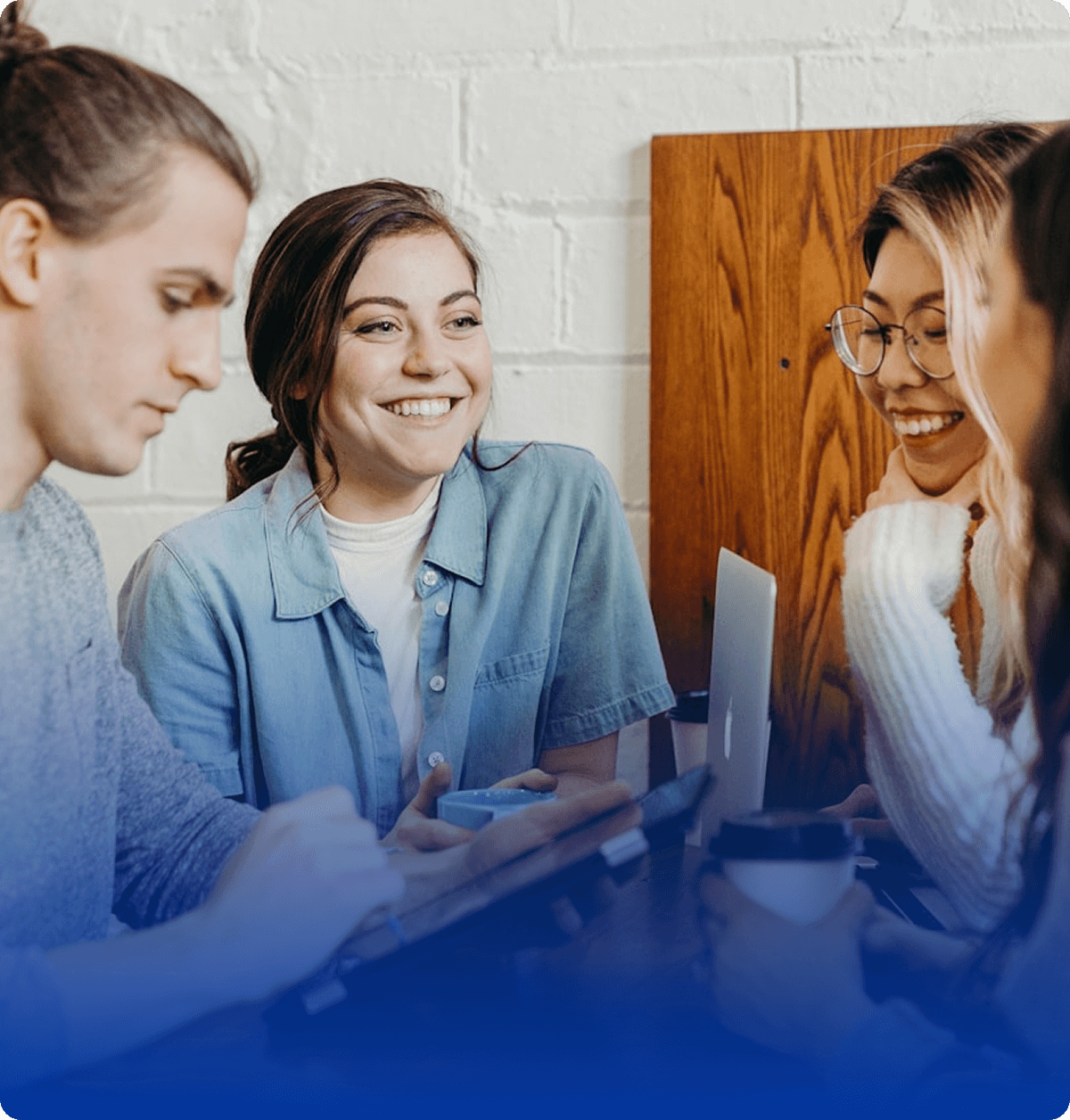 A cheerful group of coworkers collaborating in a cozy coffee shop, smiling while discussing ideas with a laptop and coffee cups on the table.