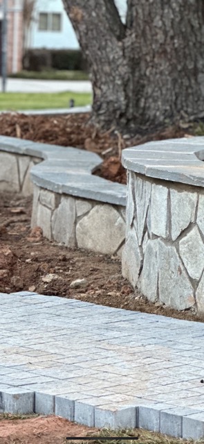 Curved stone retaining wall with a tiled cap and paved stone walkway in front.