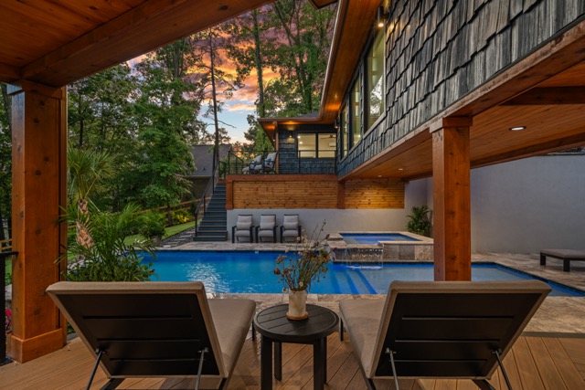 Modern backyard with pool, hot tub, deck chairs, and colorful sunset sky overhead.