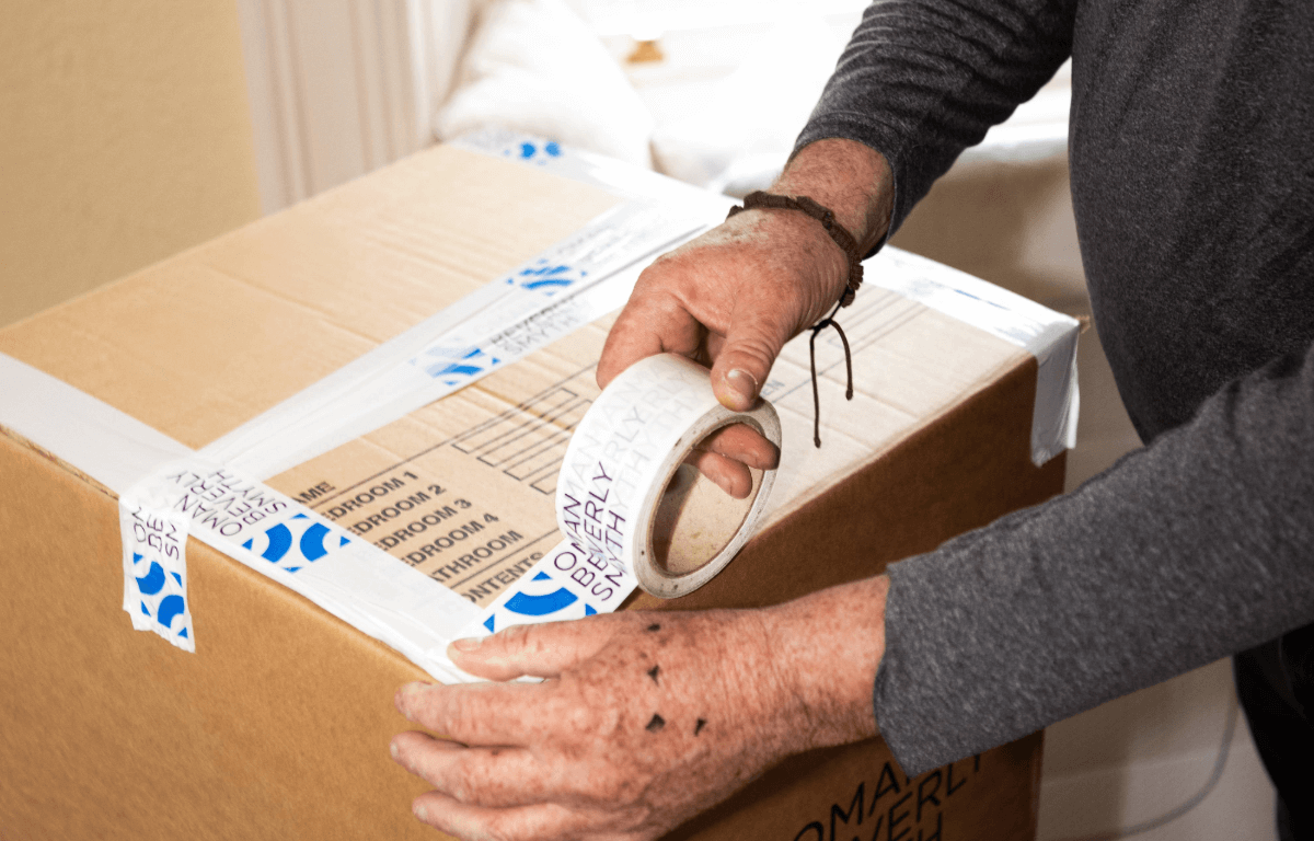 Close-up of man sealing a moving box with branded tape