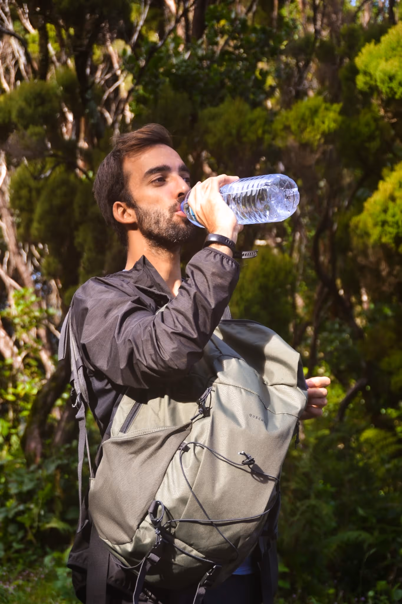 Man with backpack drinking water from a bottle while hiking in a forest.