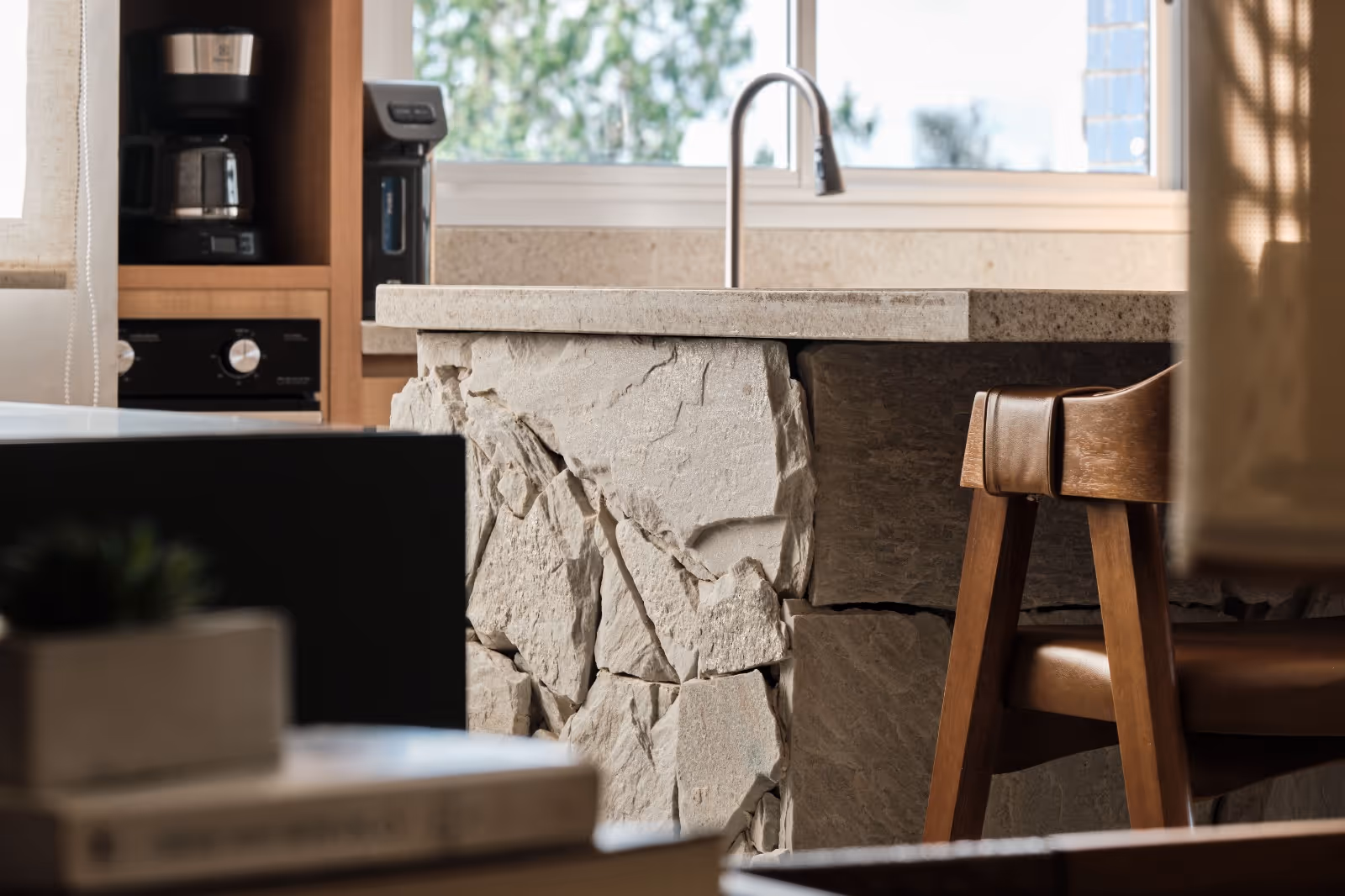 Pia de cozinha com bancada de pedra clara, cadeira de madeira e balcão com cafeteira ao fundo.