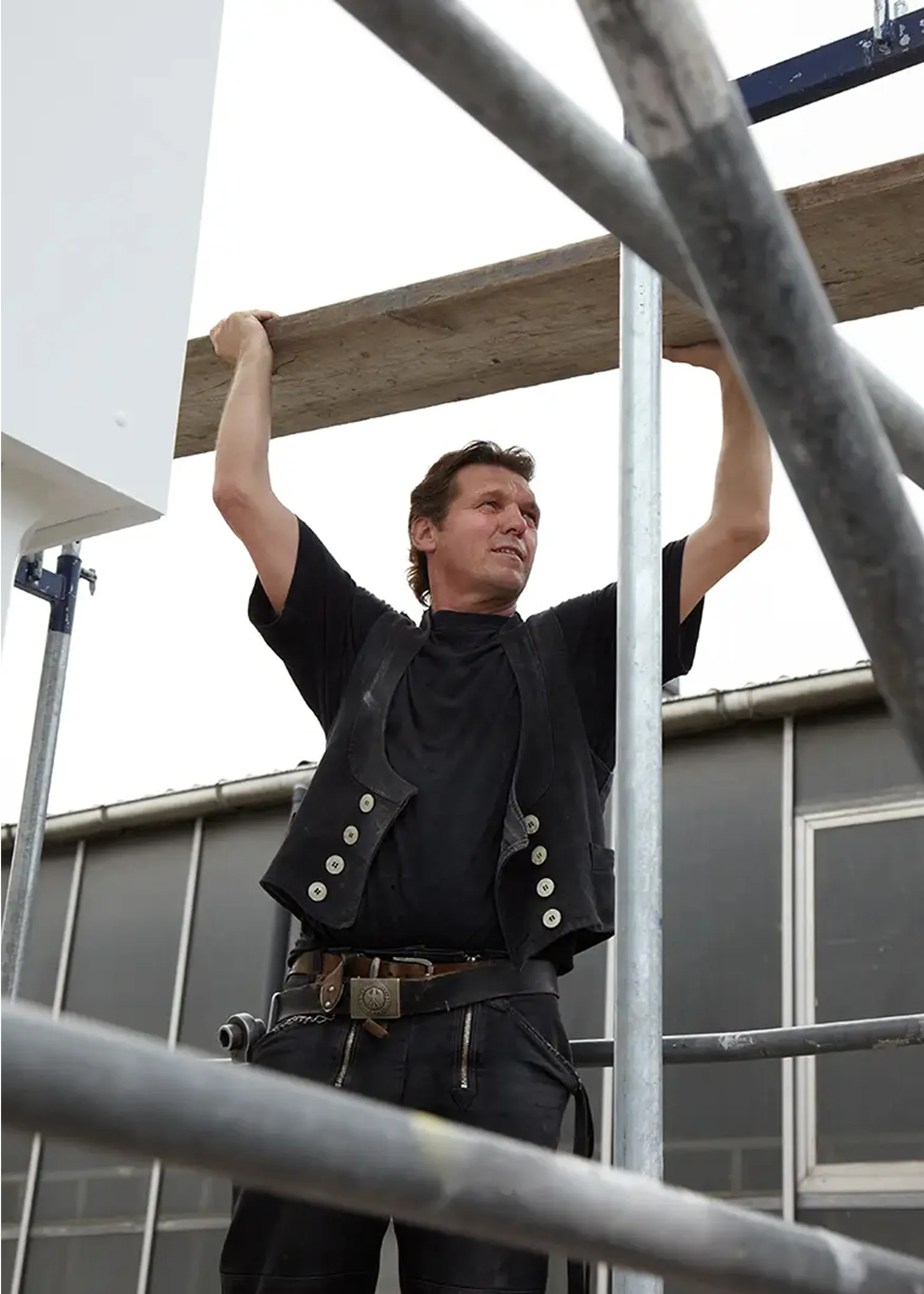 Scaffolder in black work gear standing on metal scaffolding structure at construction site