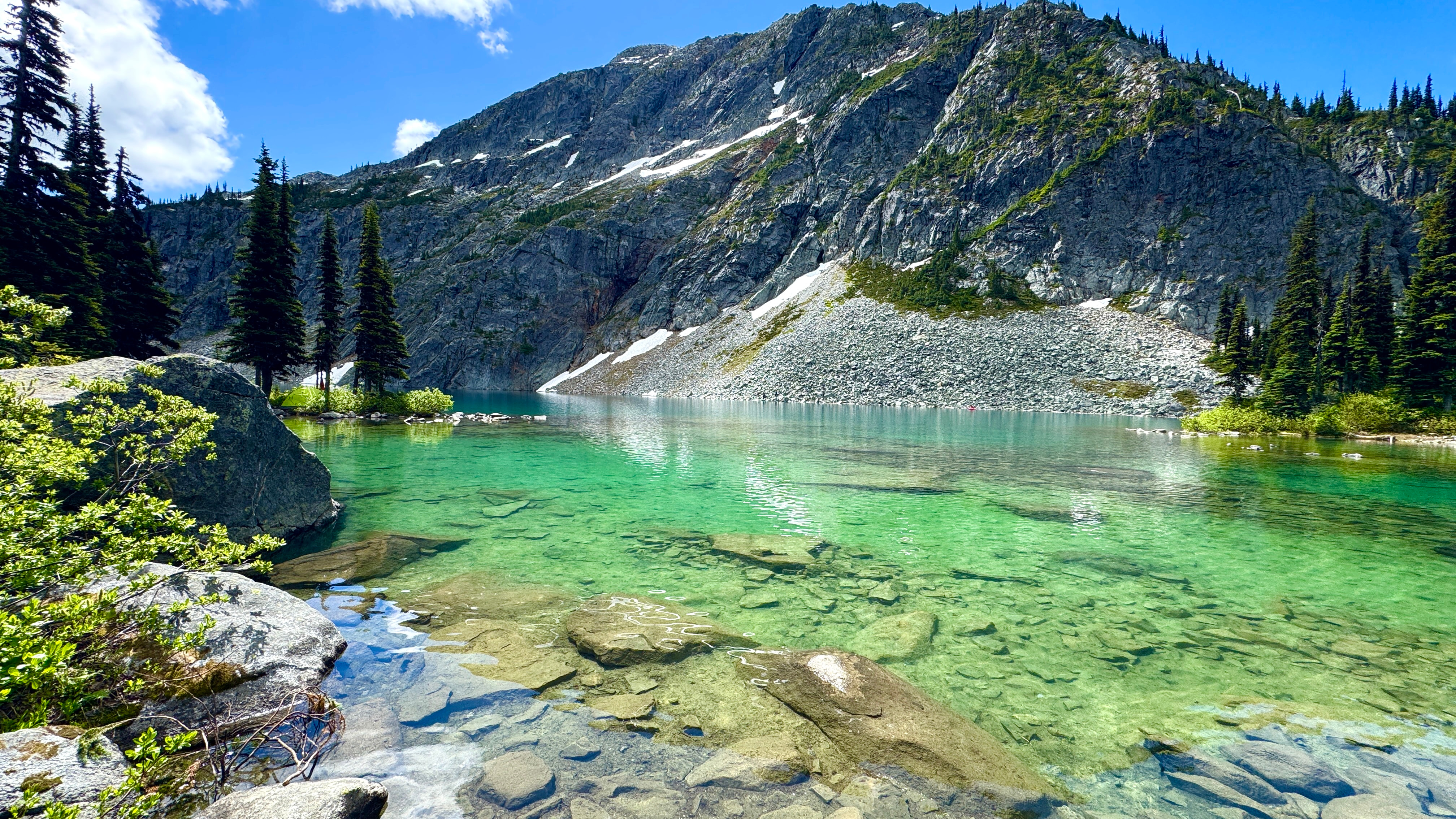 Stunning alpine lake with bright turquoise-blue water at Rohr Lake, BC, framed by steep forested mountainsides, rocky talus slopes, and tall spruce and fir trees
