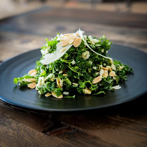 Kale salad on a black plate which is on a wooden table.