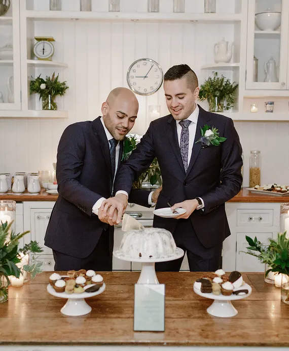 Two handsome men cutting their wedding cake in an upscale kitchen.