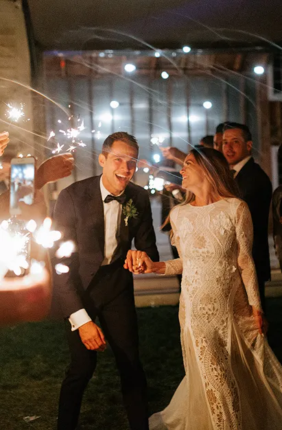 A wedding couple outside at night while friends surround them with sparklers.