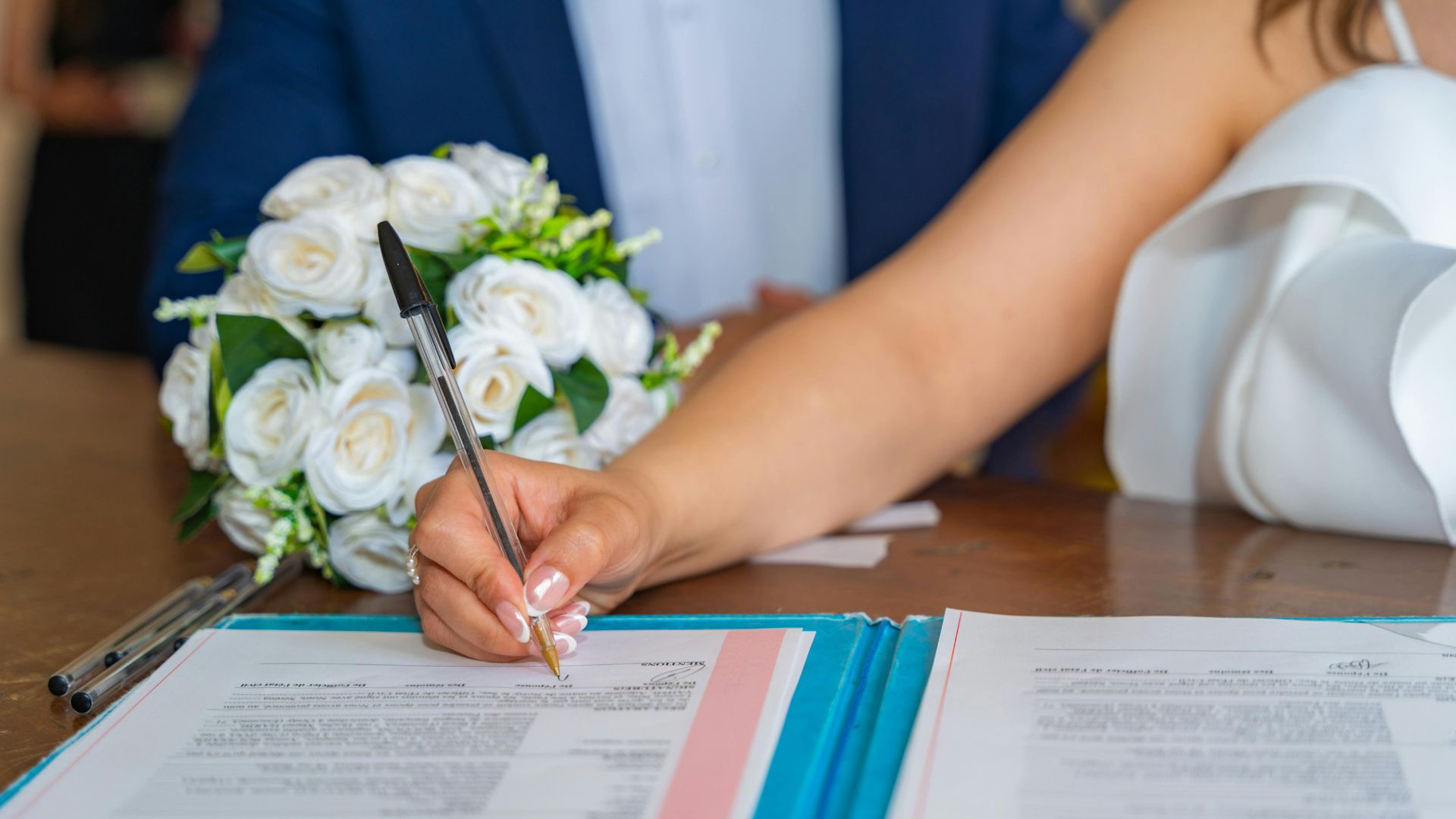 Braut unterschreibt Vertragsdokument mit Blumenstrauß im Hintergrund