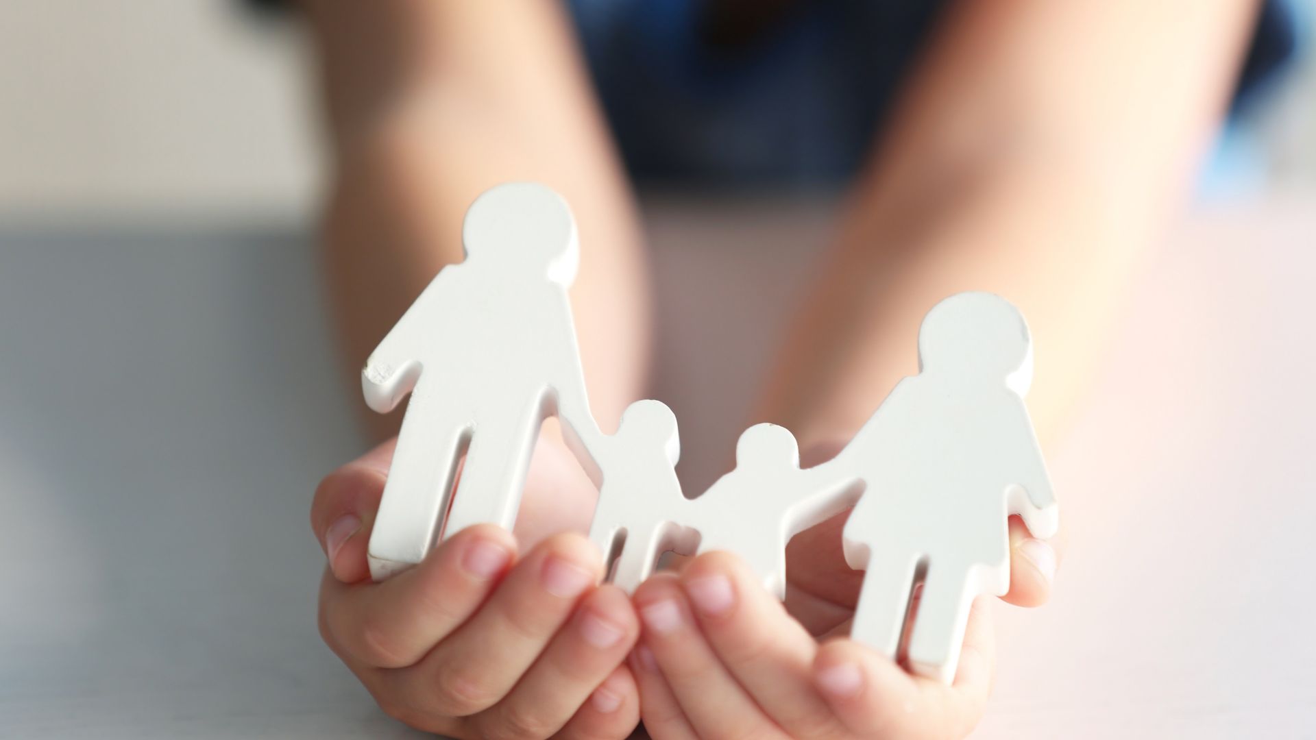 Kinderhände halten weiße Figuren einer Familie