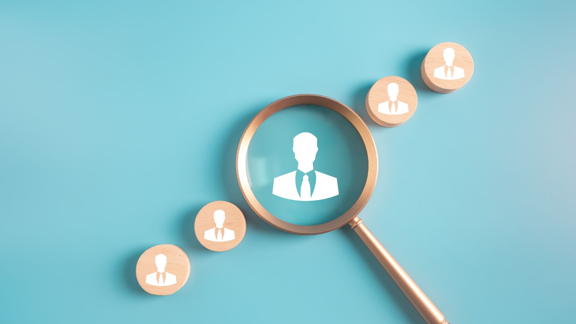 Holzfiguren mit Symbolen von Geschäftspersonen auf blauem Hintergrund, eine Lupe hebt eine Figur hervor