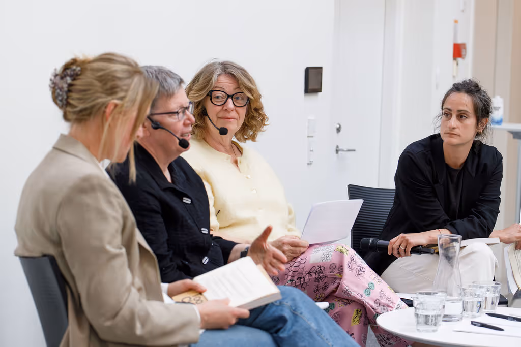 Fire kvinder i en paneldiskussion, tre har mikrofonheadsets og taler om bøger.