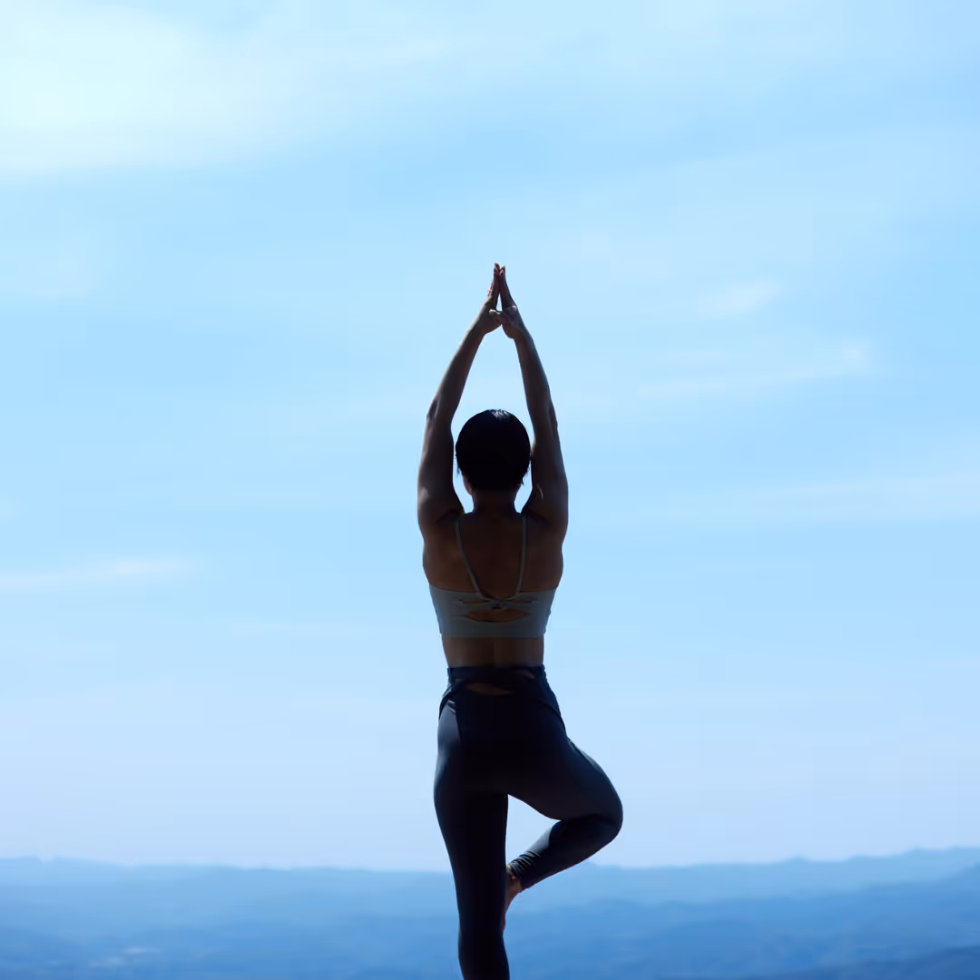 Woman practicing yoga tree pose in nature overlooking mountains during a wellness retreat