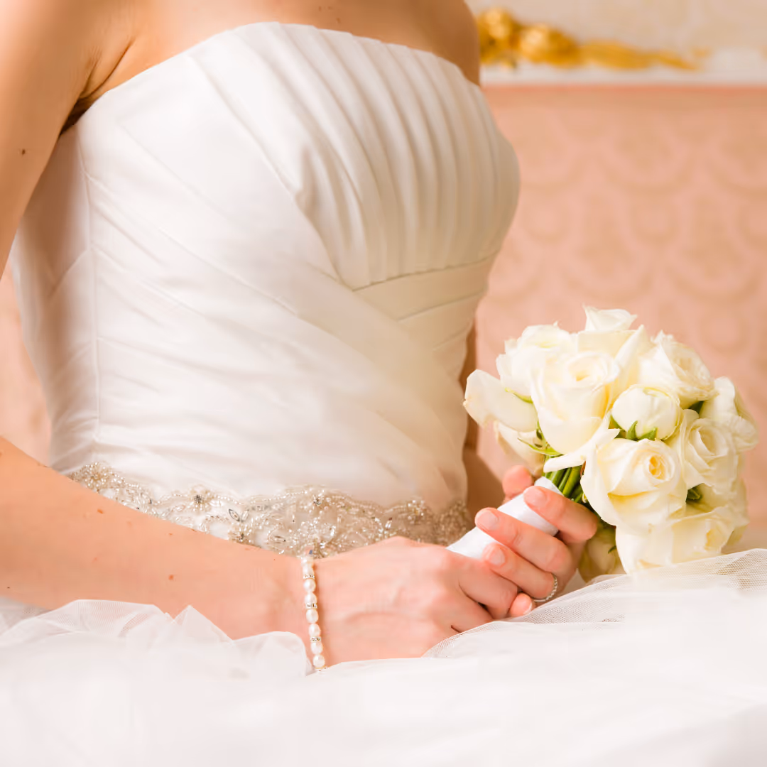 Bride in a white strapless wedding gown with bead detailing holding a bouquet of white roses.