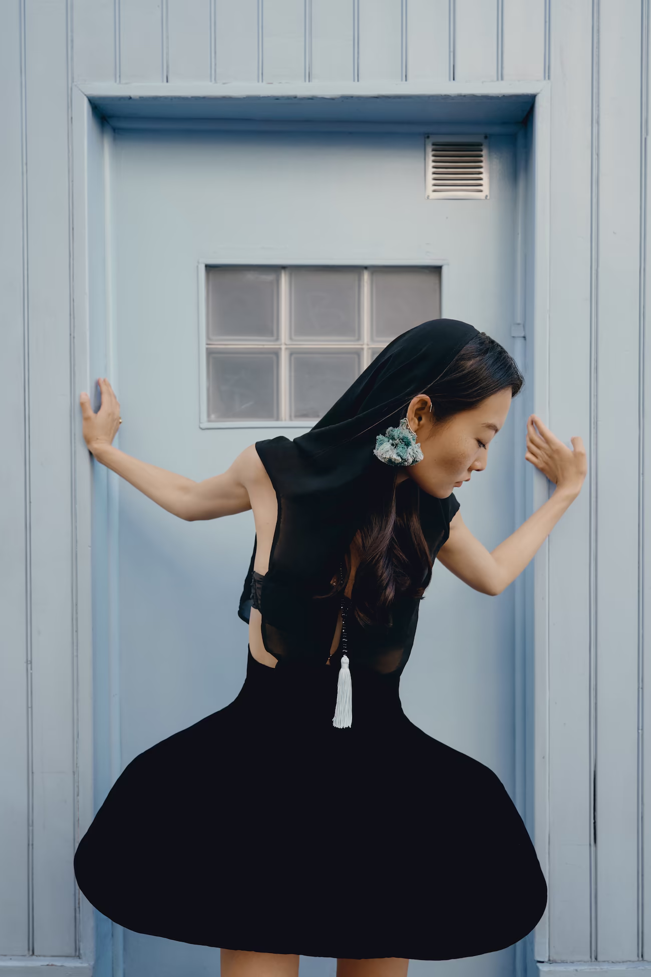 Model in a black tulip-skirted dress with statement earrings against a pale blue Parisian door — fashion editorial