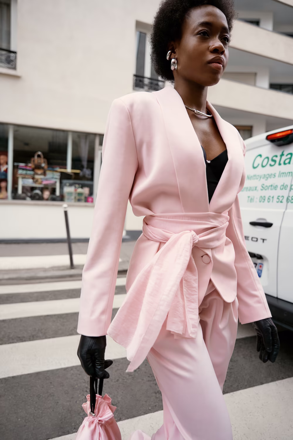 Model in a pale pink wrap blazer crossing a Paris street — fashion editorial