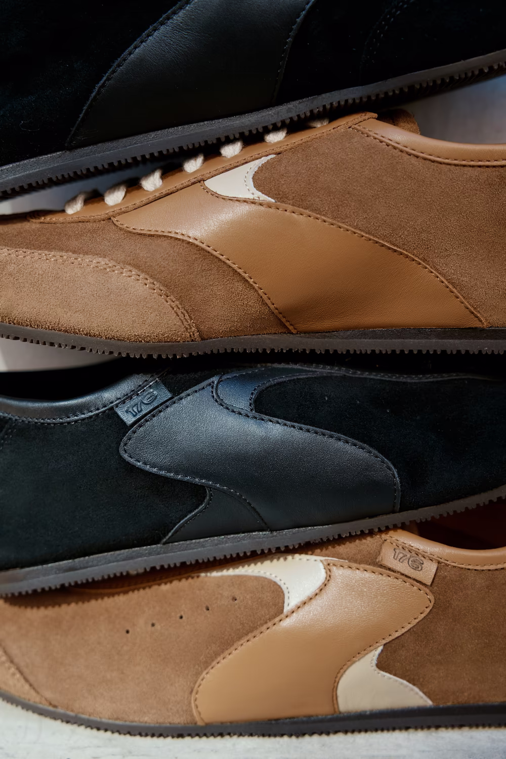 Close-up still life of stacked suede and leather sneakers in tan, black and cream — footwear product photography