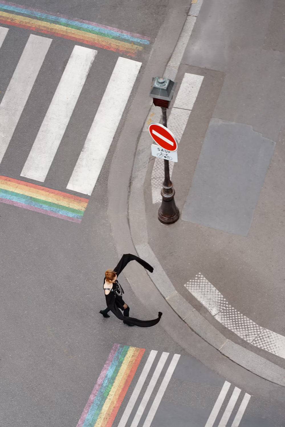 Overhead of a rainbow-painted pedestrian crossing with a cyclist passing a no-entry sign — urban brand photography