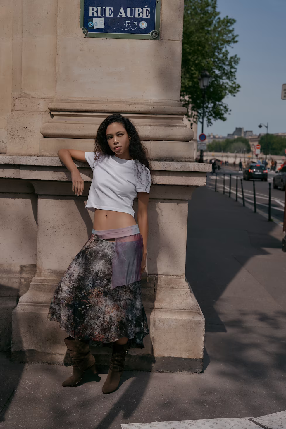 Model in a white crop tee and printed sheer maxi skirt under the Rue Aubé street sign in Paris — fashion campaign