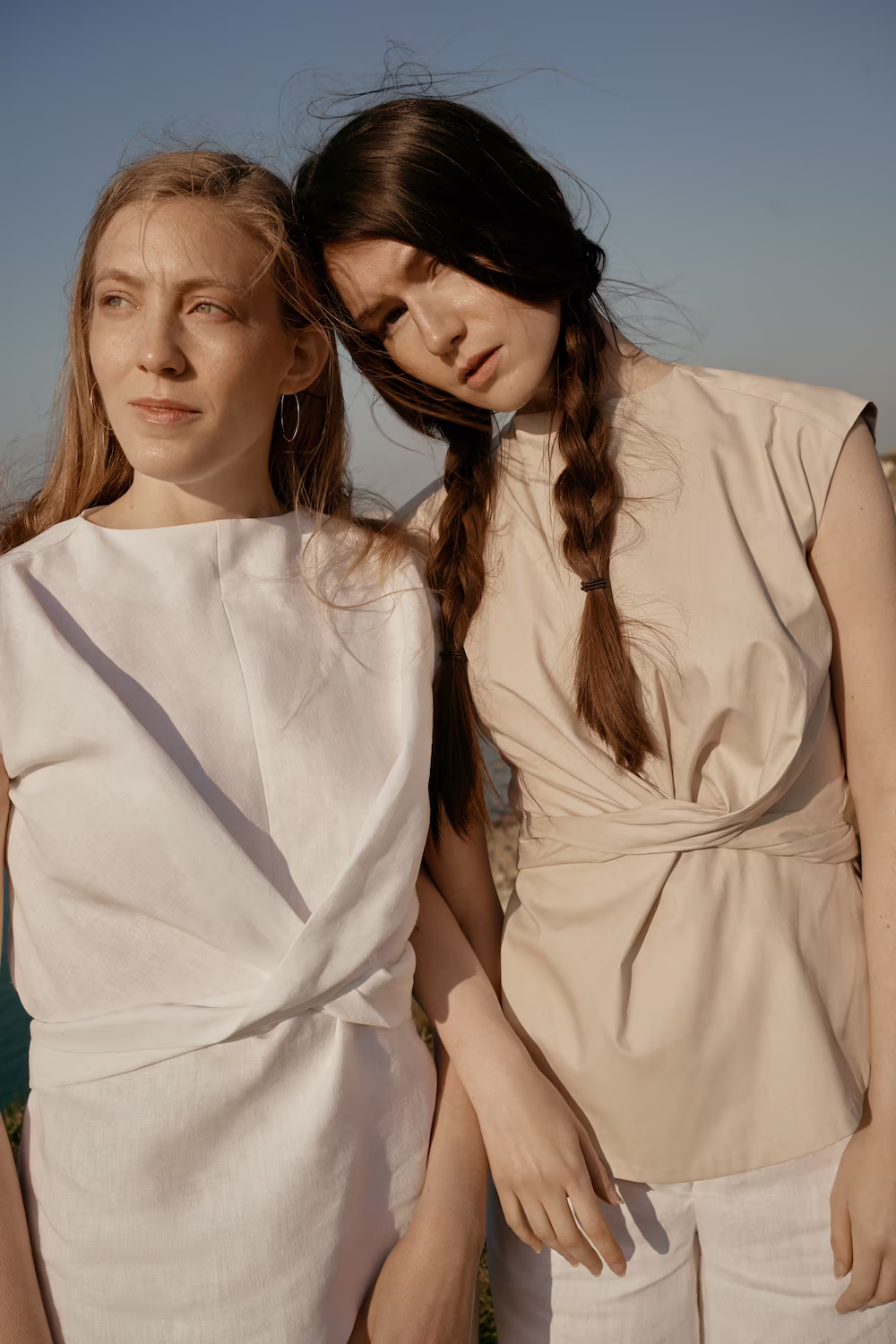 Two models in cream and beige linen looks standing close together, hair windswept — fashion campaign