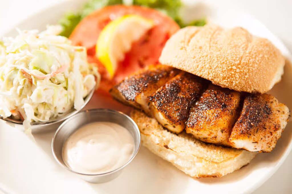 A plate of food with a sandwich, coleslaw, and a pickle.
