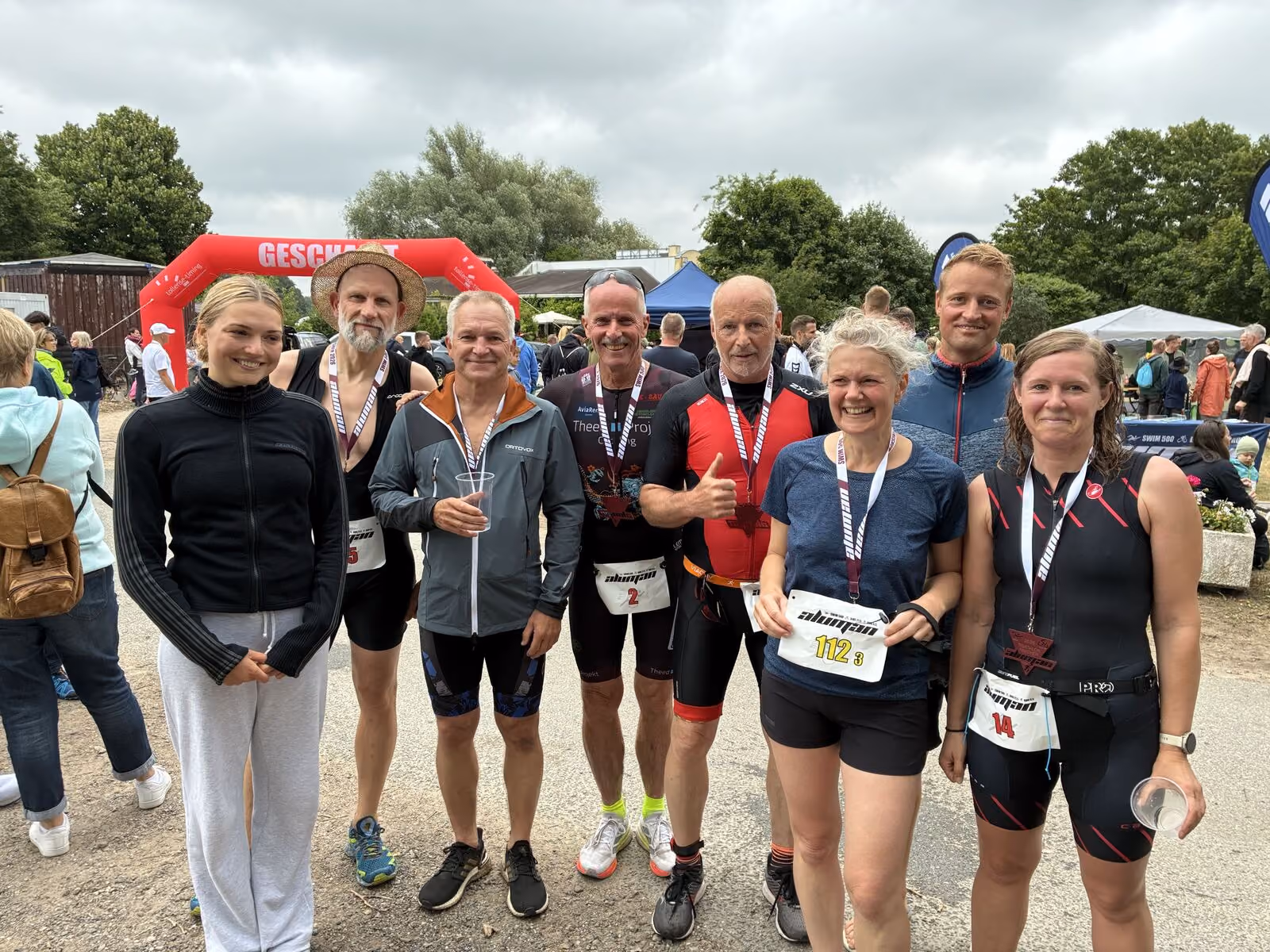 Acht Menschen in Sportkleidung posieren lächelnd nach einem Wettkampf im Freien.