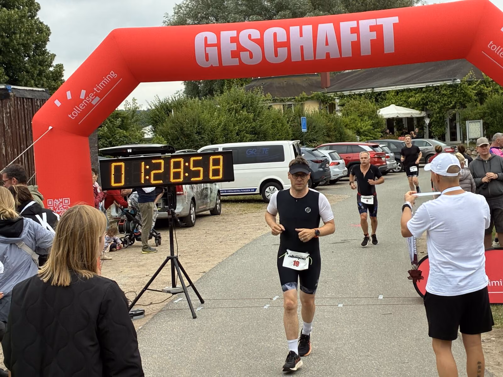 Männer laufen unter einem roten aufblasbaren Zielbogen mit der Aufschrift ‚Geschafft‘ bei einem Rennen.