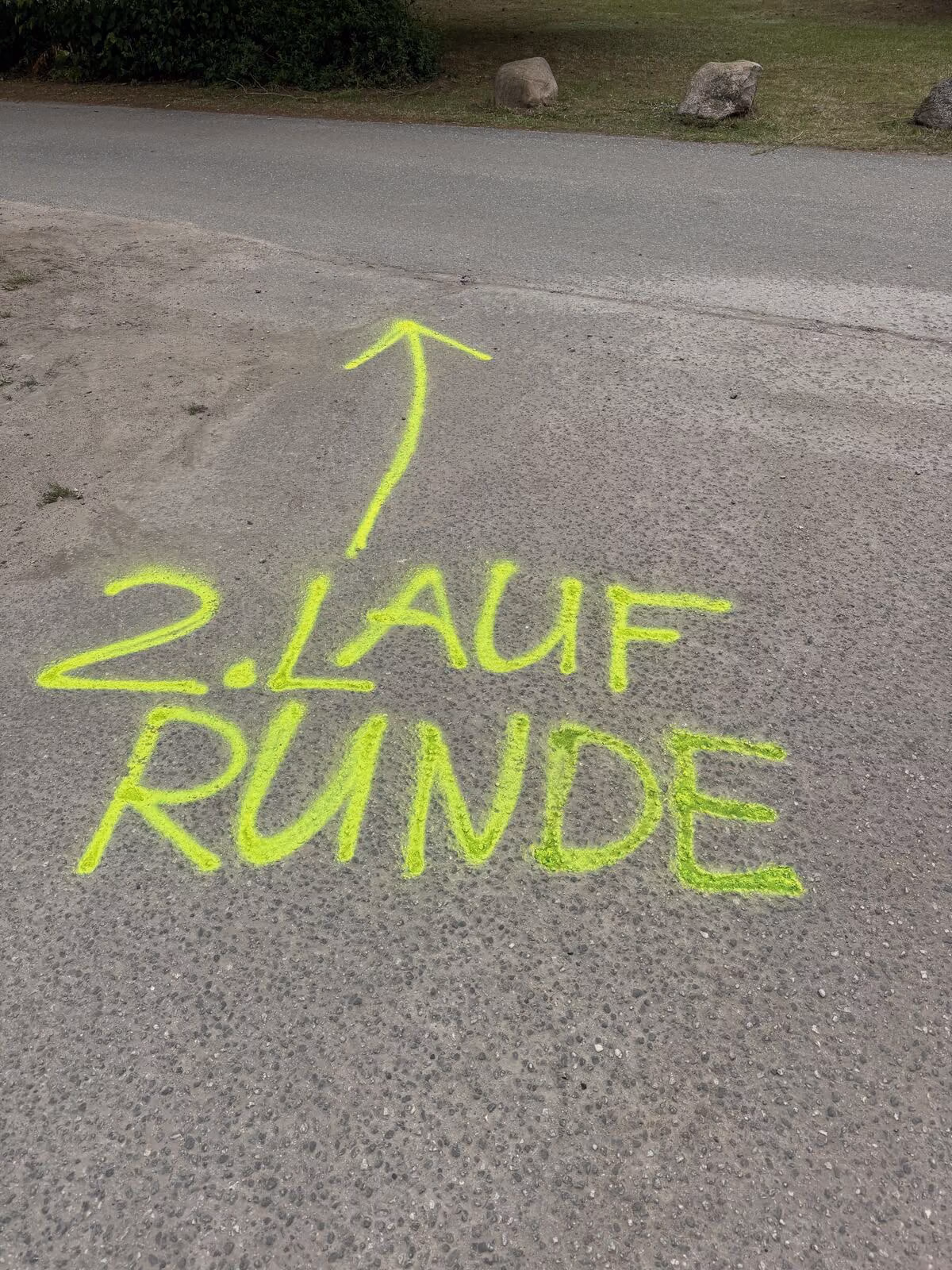 Gelbe Markierung auf Asphalt mit Pfeil und Text: 2. Lauf Runde.