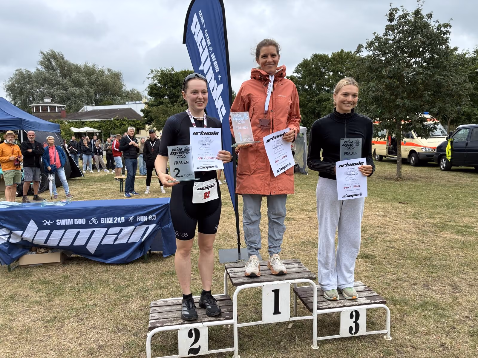 Drei Frauen stehen auf Gewinnerpodest mit Urkunden bei einem Mehrkampf-Event im Freien.