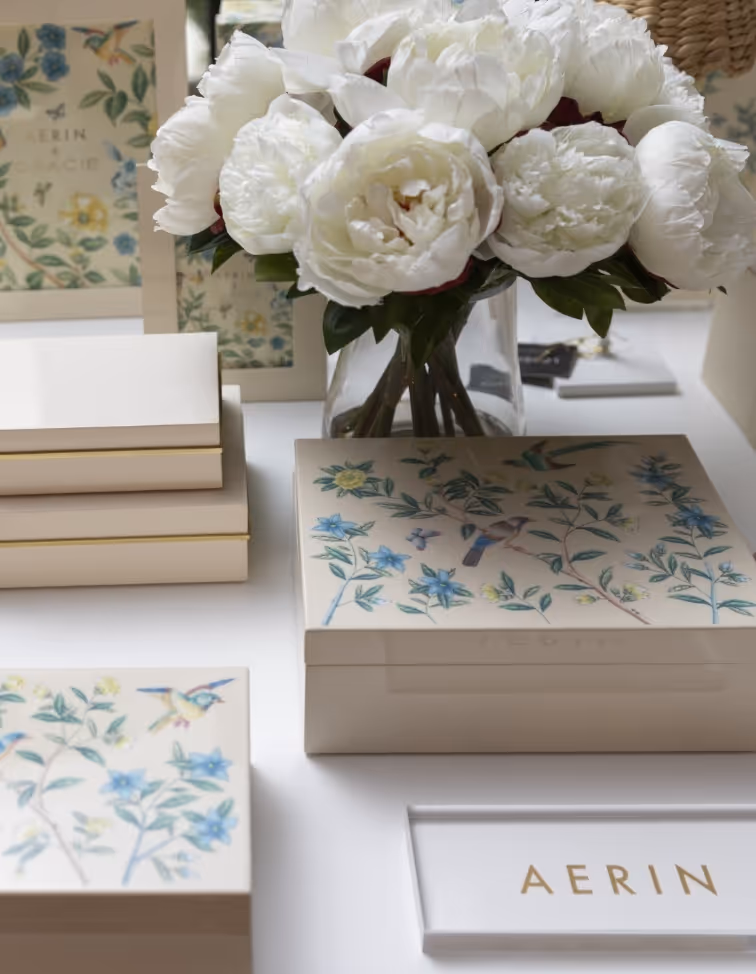 Tabletop display of AERIN-branded boxes and photo frames with a vase of fresh flowers near The St. Regis Houston. 